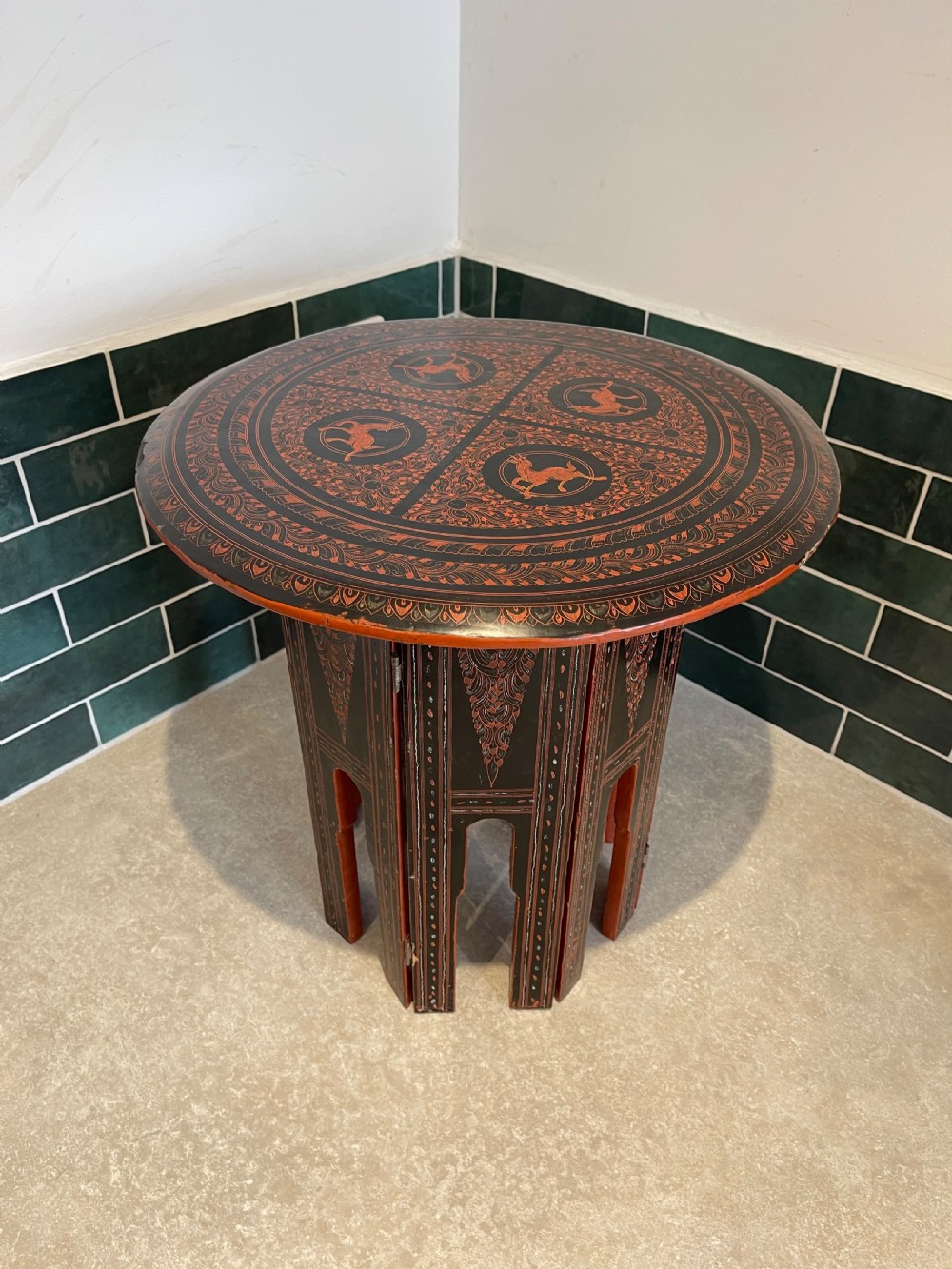 An octagonal Burmese lacquered folding side table featuring black and red panels decorated with incised geometric and floral motifs above arched openwork legs. View II