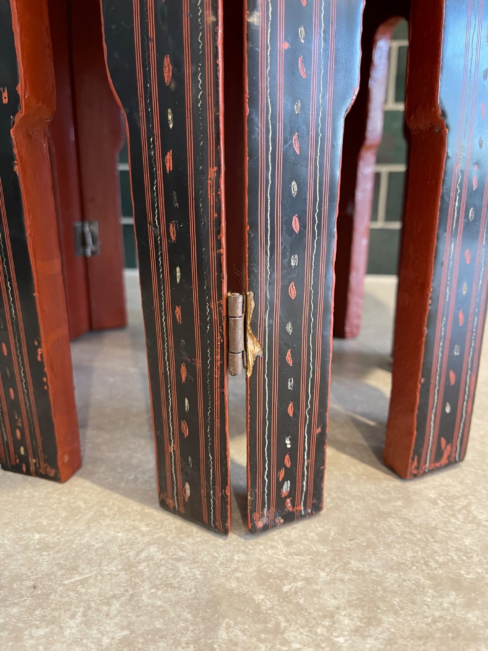 An octagonal Burmese lacquered folding side table featuring black and red panels decorated with incised geometric and floral motifs above arched openwork legs. View V
