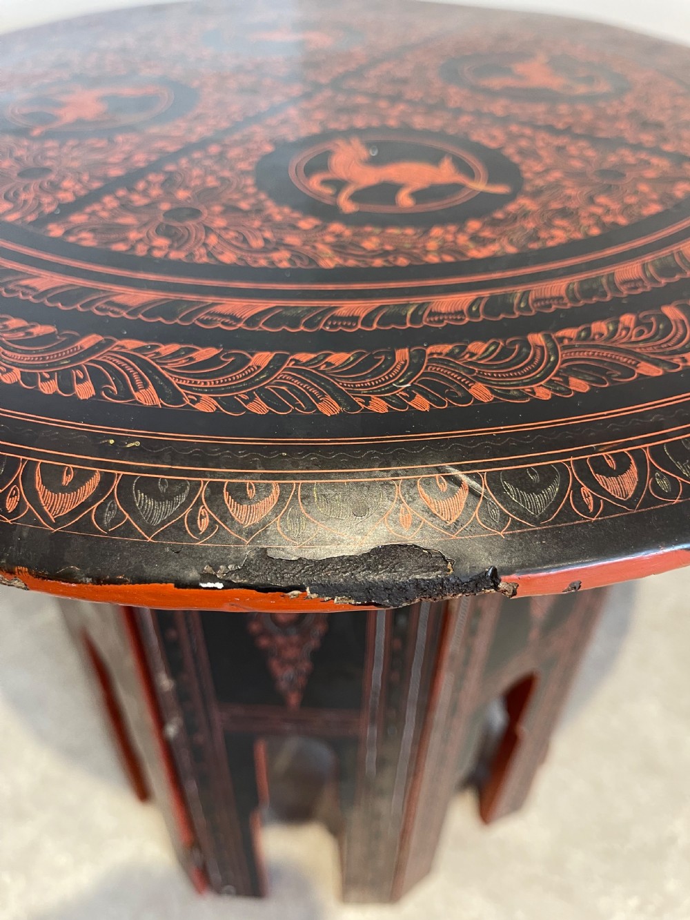 An octagonal Burmese lacquered folding side table featuring black and red panels decorated with incised geometric and floral motifs above arched openwork legs. View VI
