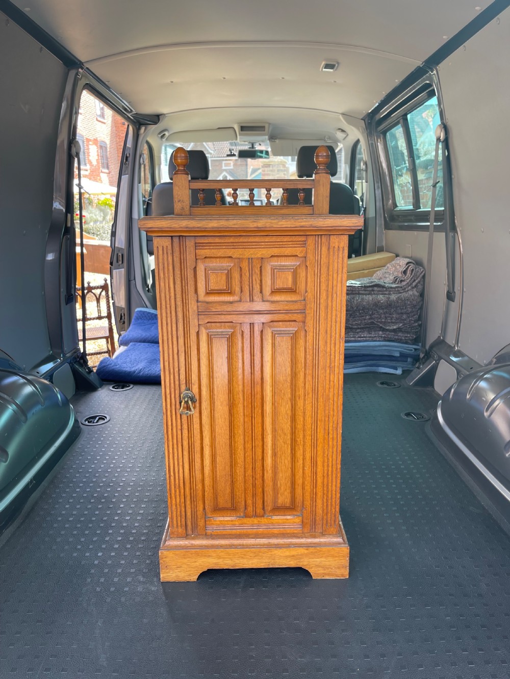 A late Victorian oak bedside cupboard featuring a turned spindle gallery top and a fielded panel single door with a brass handle.