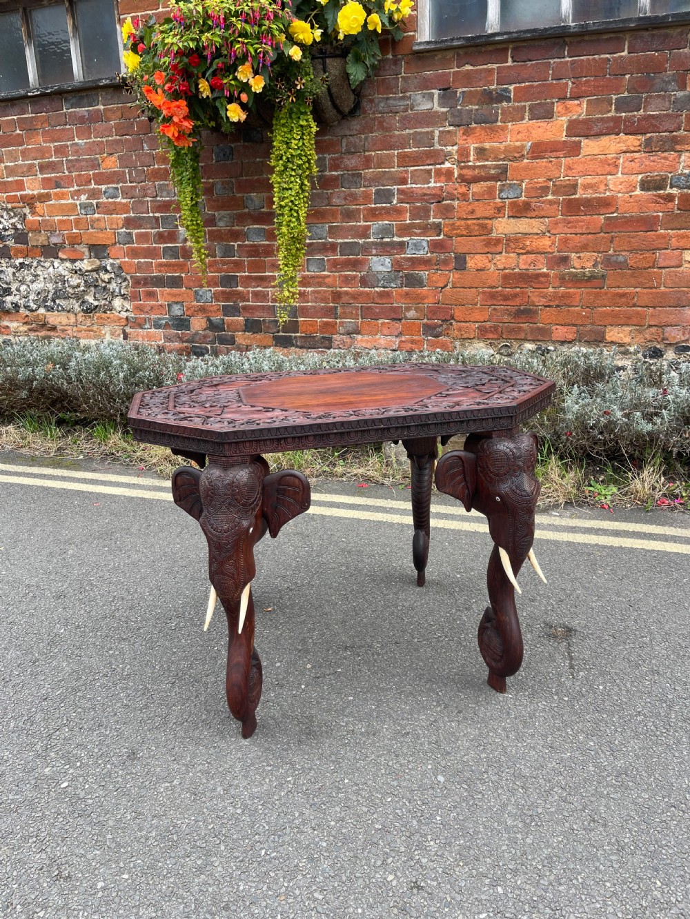 A dark brown carved wood occasional table featuring an octagonal top and three legs sculpted into detailed elephant heads with light tusks.