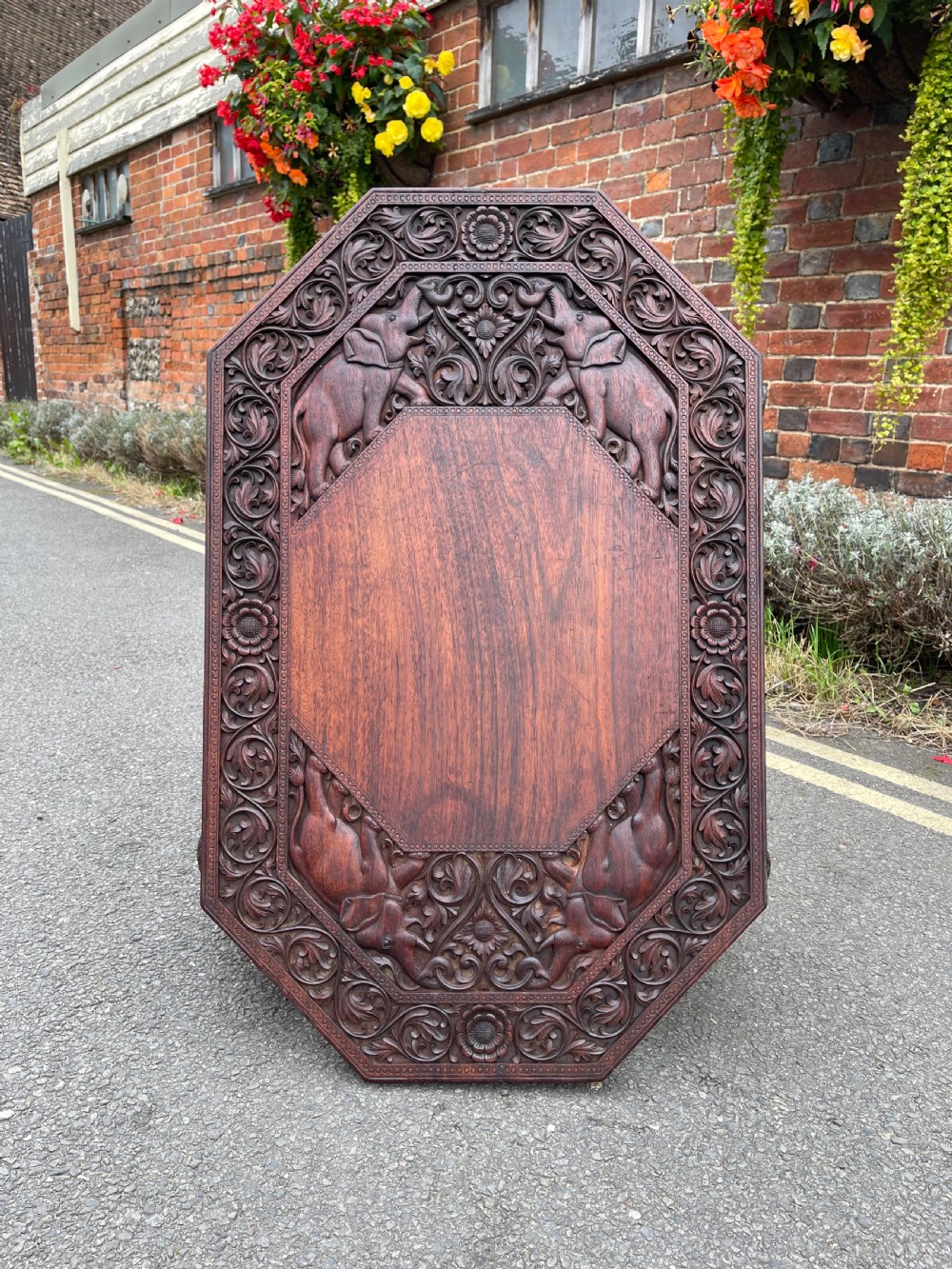 A dark brown carved wood occasional table featuring an octagonal top and three legs sculpted into detailed elephant heads with light tusks. View III