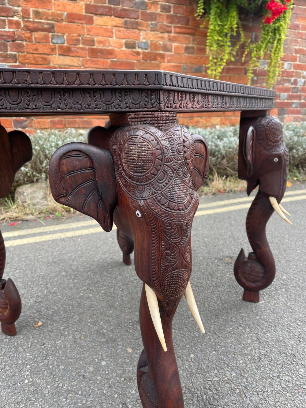 A dark brown carved wood occasional table featuring an octagonal top and three legs sculpted into detailed elephant heads with light tusks. View V