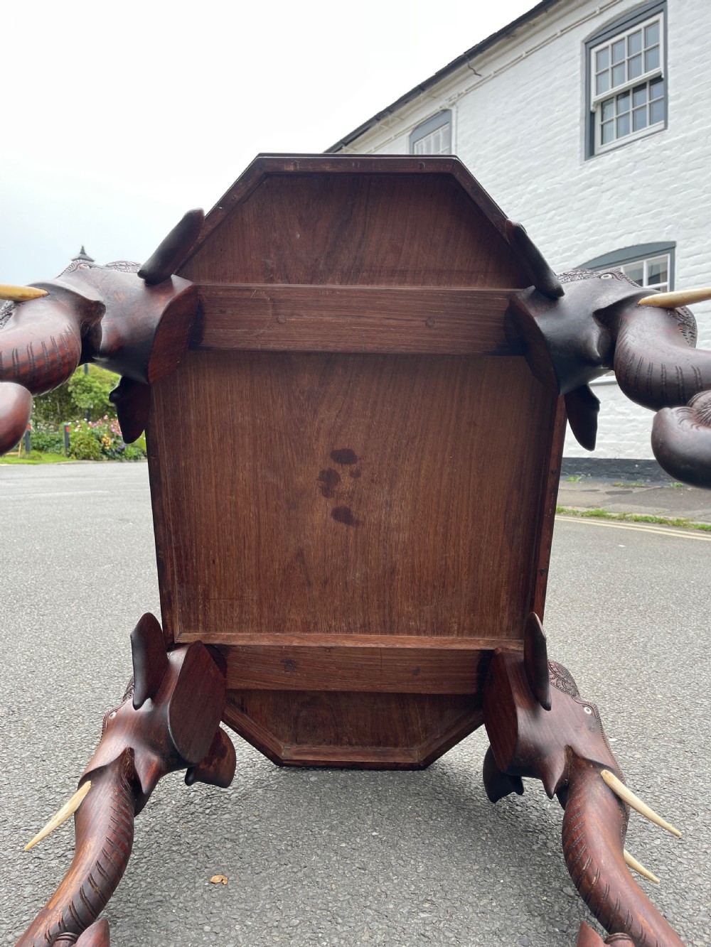 A dark brown carved wood occasional table featuring an octagonal top and three legs sculpted into detailed elephant heads with light tusks. View VI
