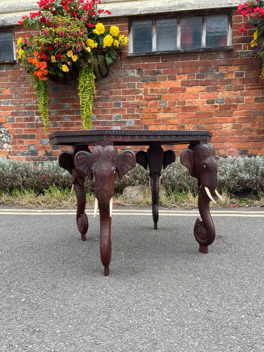 A dark brown carved wood occasional table featuring an octagonal top and three legs sculpted into detailed elephant heads with light tusks. View VII