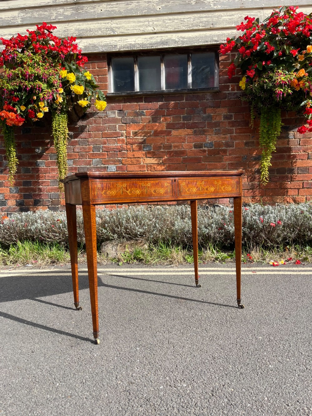 A late Victorian satinwood bijouterie table featuring a glazed display top, floral marquetry inlay along the frieze, and tapered legs with brass castors. View III