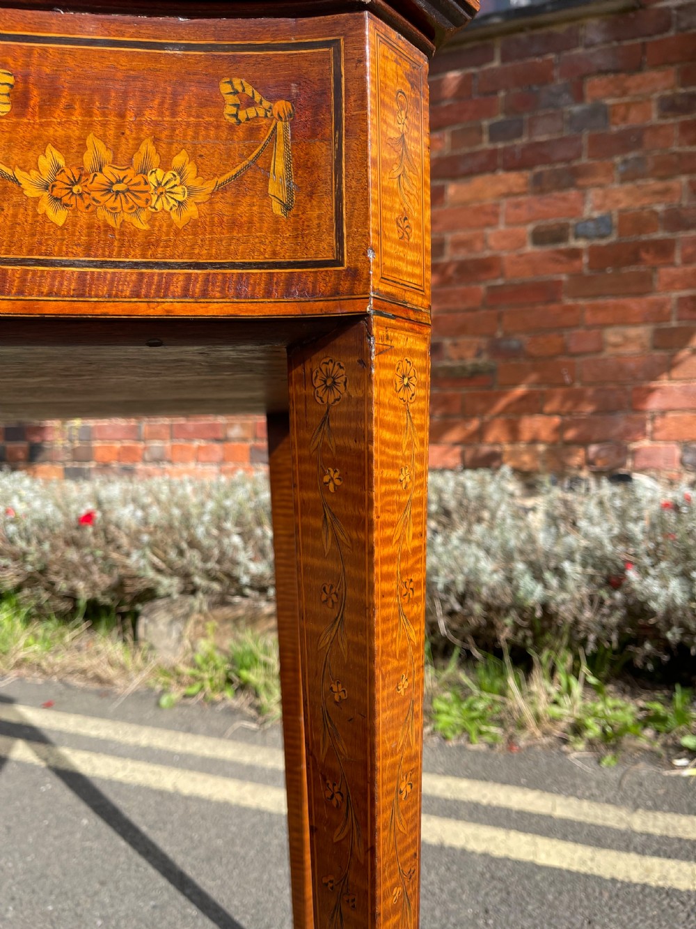 A late Victorian satinwood bijouterie table featuring a glazed display top, floral marquetry inlay along the frieze, and tapered legs with brass castors. View V