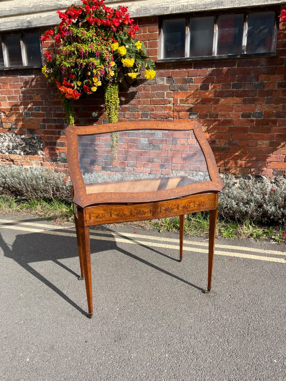 A late Victorian satinwood bijouterie table featuring a glazed display top, floral marquetry inlay along the frieze, and tapered legs with brass castors. View XII