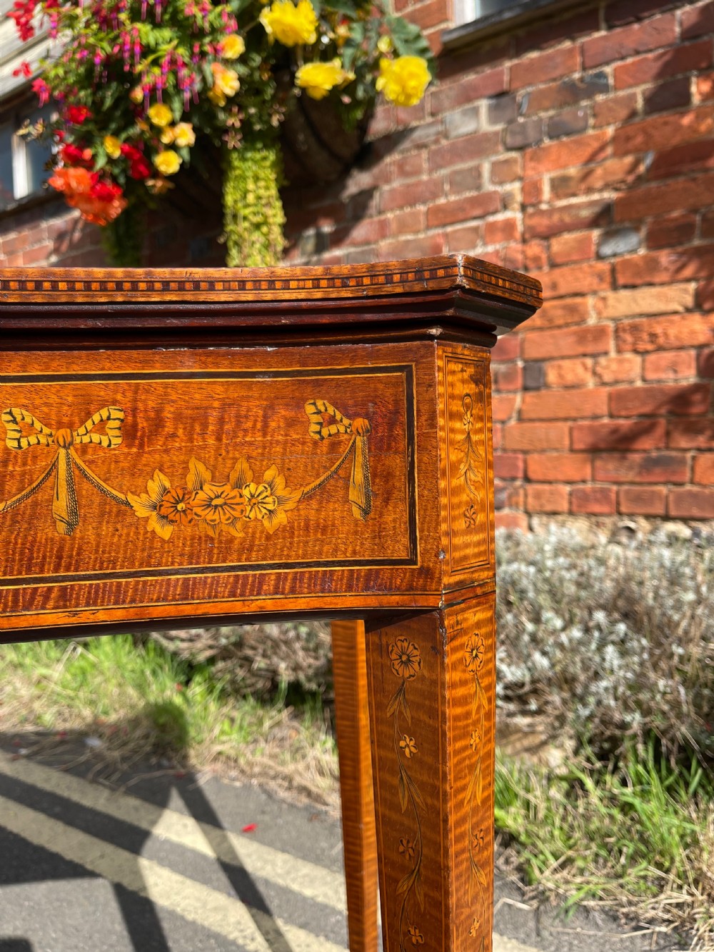 A late Victorian satinwood bijouterie table featuring a glazed display top, floral marquetry inlay along the frieze, and tapered legs with brass castors. View XIV