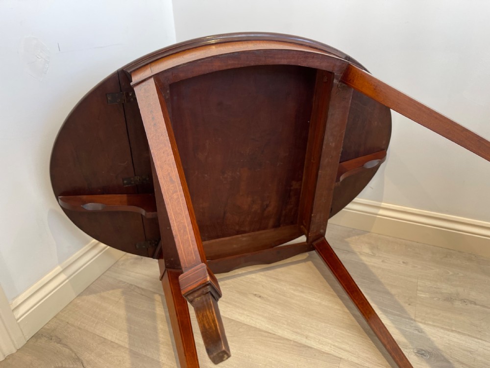 An oval antique mahogany Pembroke table with detailed marquetry inlay, drop leaves, and tapered legs. View V