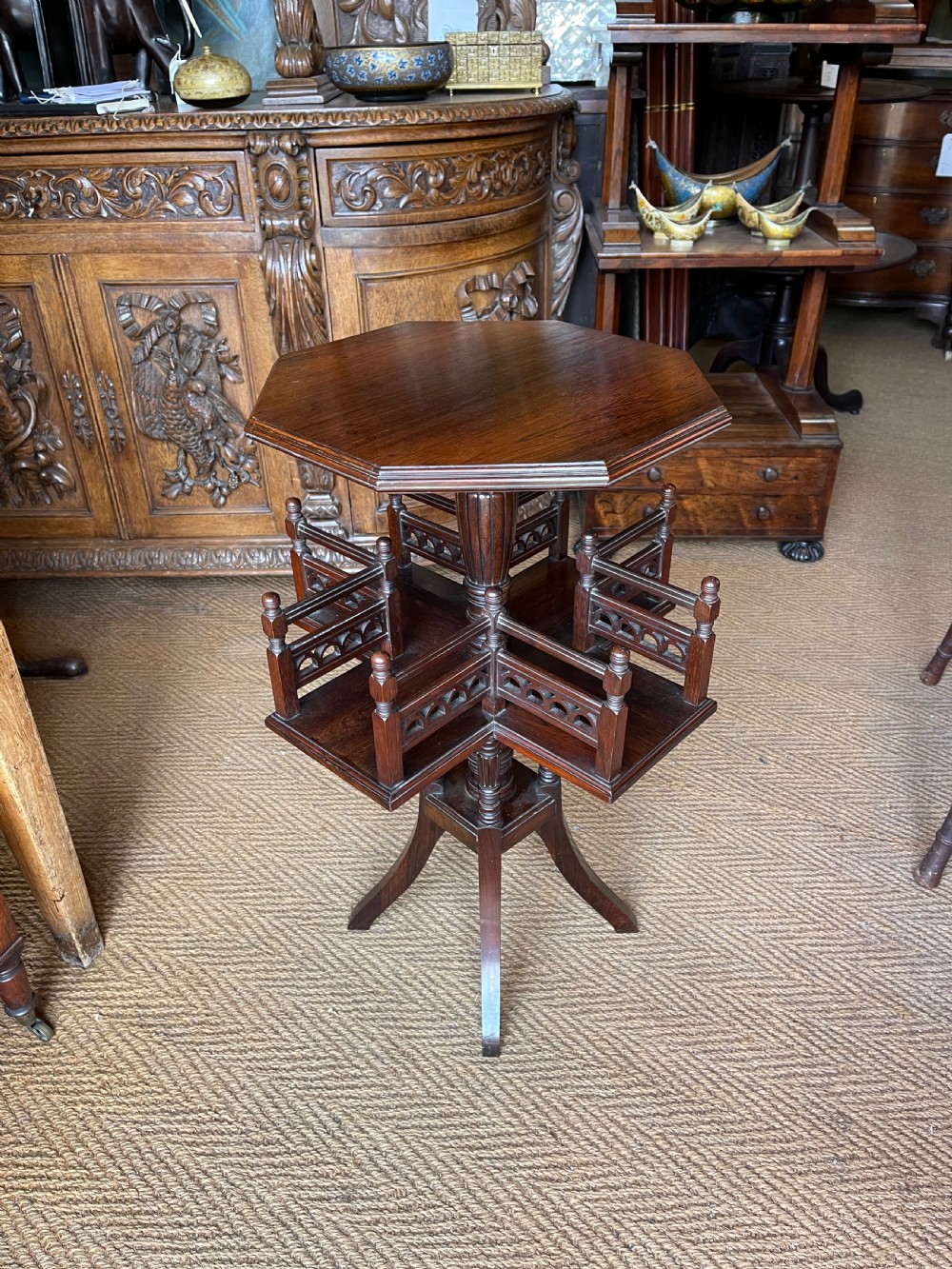 A nineteenth-century rosewood revolving book table featuring an octagonal top, pierced fretwork gallery compartments, turned central column, and four swept legs.