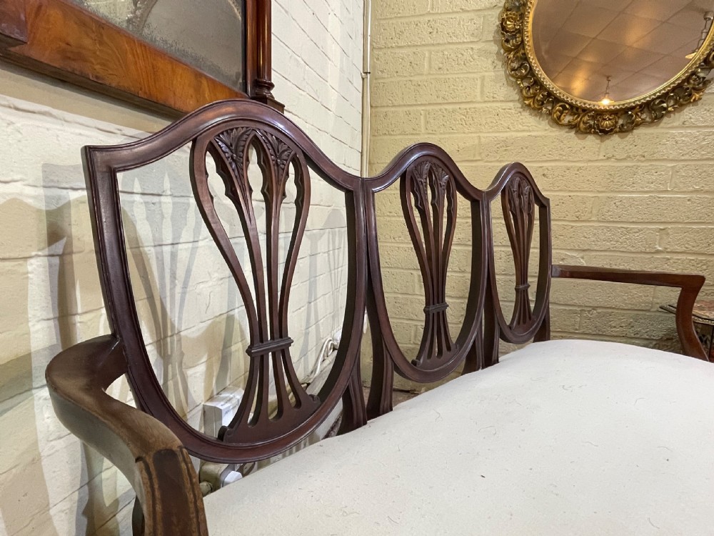 A dark mahogany triple chair-back settee with three pierced shield-shaped splats, swept armrests, square legs, and a neutral cream upholstered seat. View II