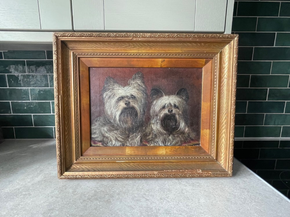 An oil painting on canvas depicting two shaggy terriers set within a wide, gilt wooden frame.