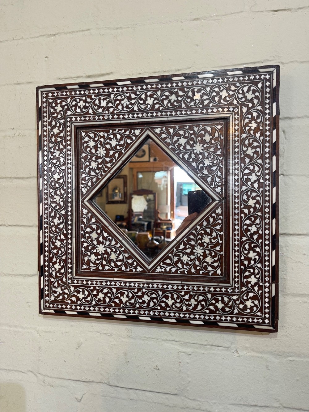 A square dark wood Anglo-Indian Hoshiarpur mirror featuring intricate bone inlay floral scrollwork surrounding a diamond-shaped central glass aperture.