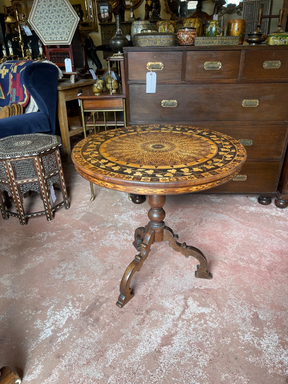A nineteenth-century circular wooden table with a central starburst marquetry top, floral border, turned pedestal, and tripod legs.