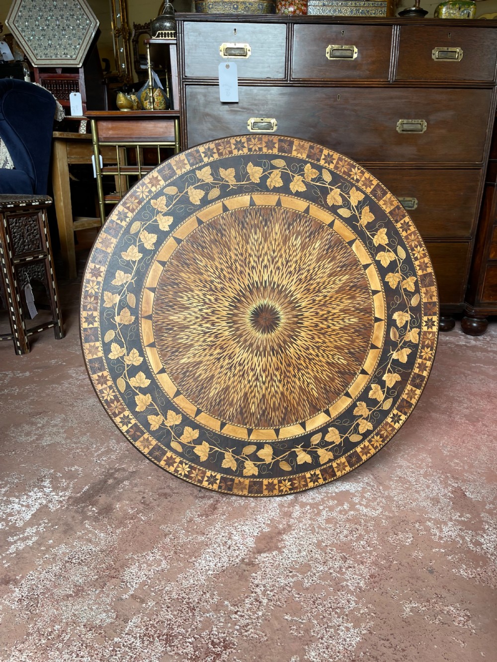 A nineteenth-century circular wooden table with a central starburst marquetry top, floral border, turned pedestal, and tripod legs. View II