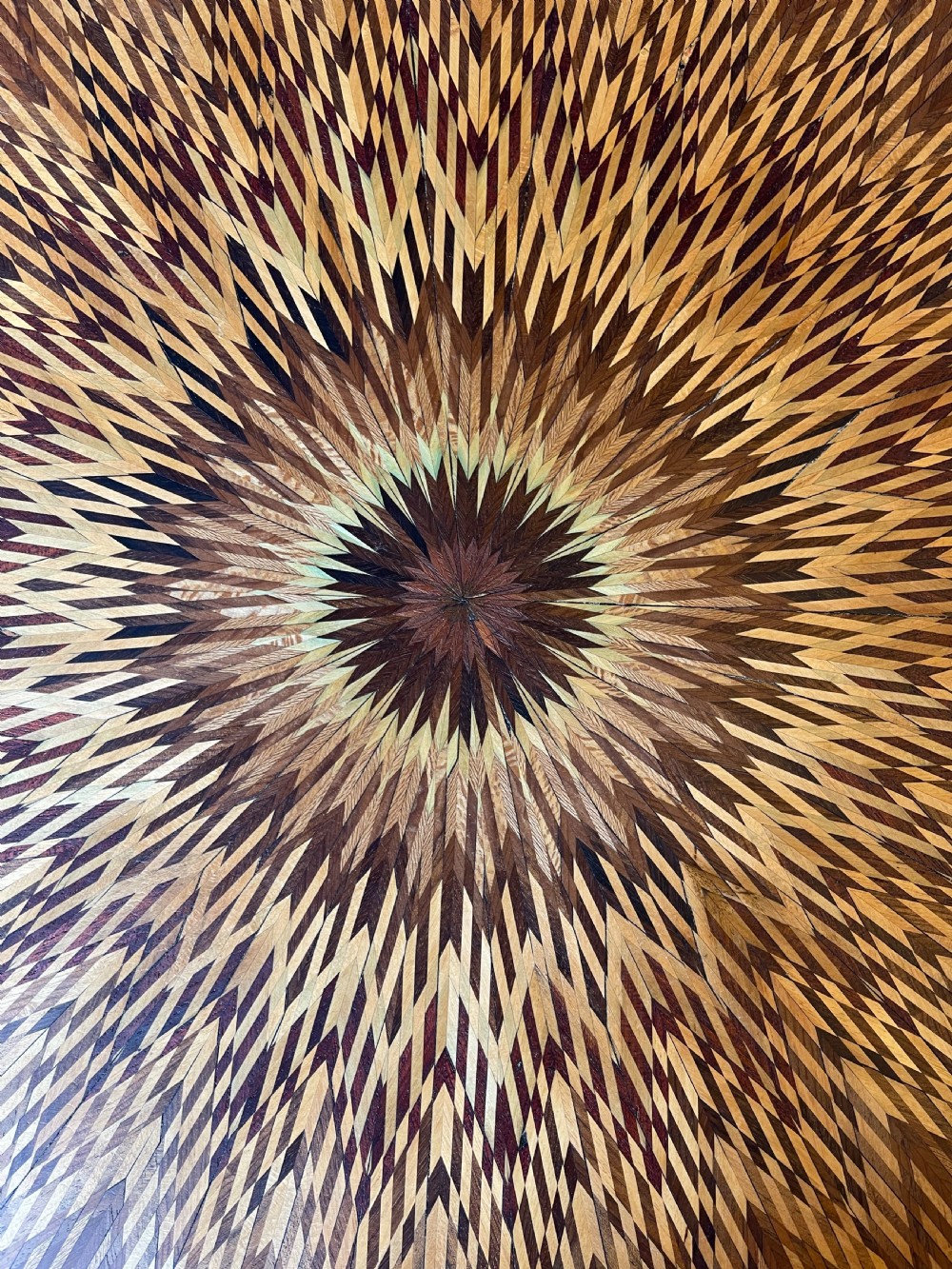 A nineteenth-century circular wooden table with a central starburst marquetry top, floral border, turned pedestal, and tripod legs. View III
