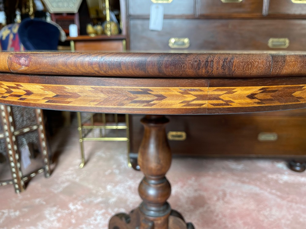 A nineteenth-century circular wooden table with a central starburst marquetry top, floral border, turned pedestal, and tripod legs. View V