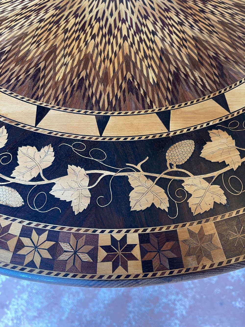 A nineteenth-century circular wooden table with a central starburst marquetry top, floral border, turned pedestal, and tripod legs. View VI