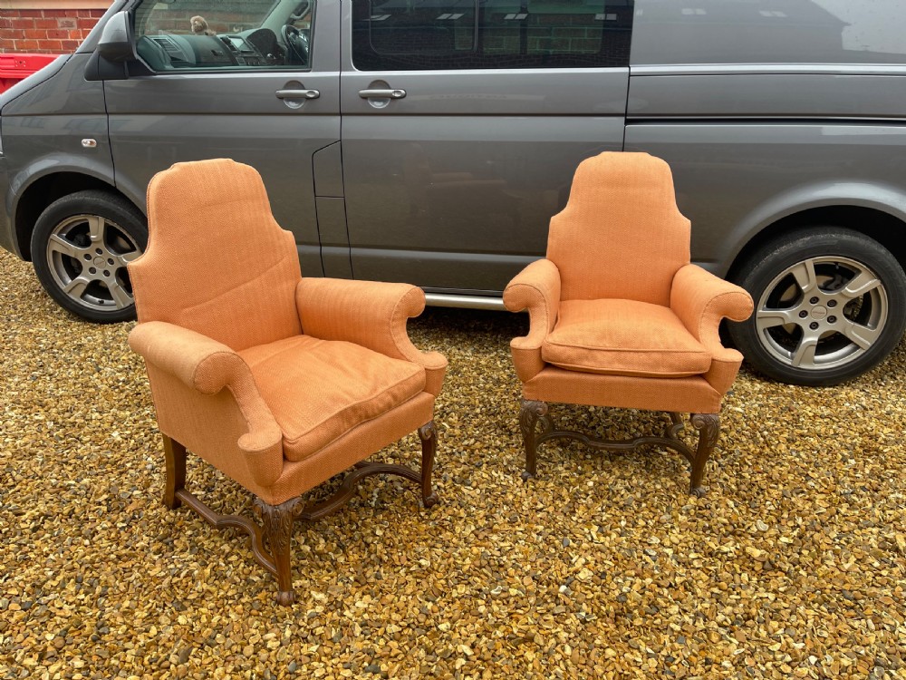 A pair of high-backed armchairs upholstered in textured orange fabric with intricate carved walnut legs and serpentine stretchers.