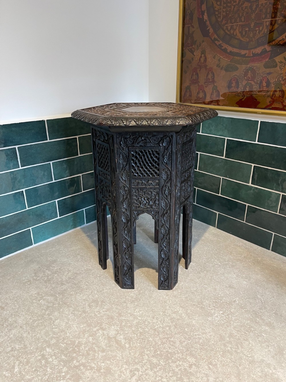 An octagonal dark wood side table with intricate hand-carved foliate patterns and openwork lattice panels on the base.