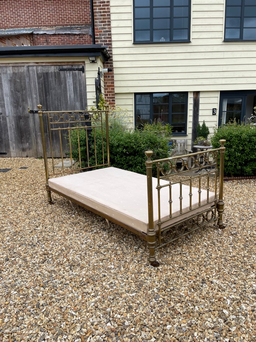 A Victorian single brass bed frame featuring a tall headboard and shorter footboard with turned finials and decorative circular ring inserts, set on castors.