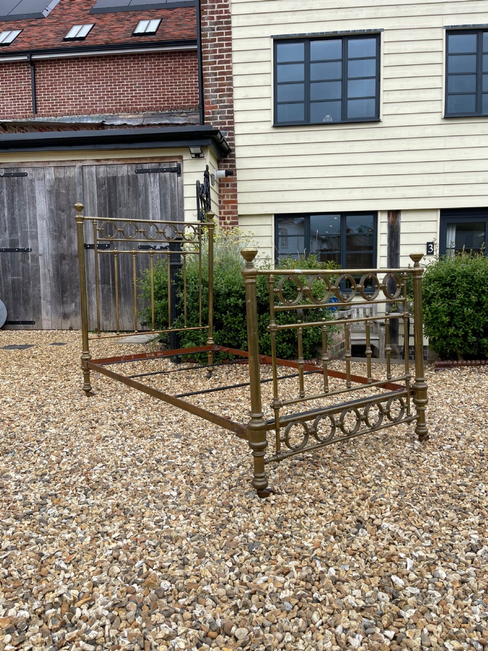 A Victorian single brass bed frame featuring a tall headboard and shorter footboard with turned finials and decorative circular ring inserts, set on castors. View III