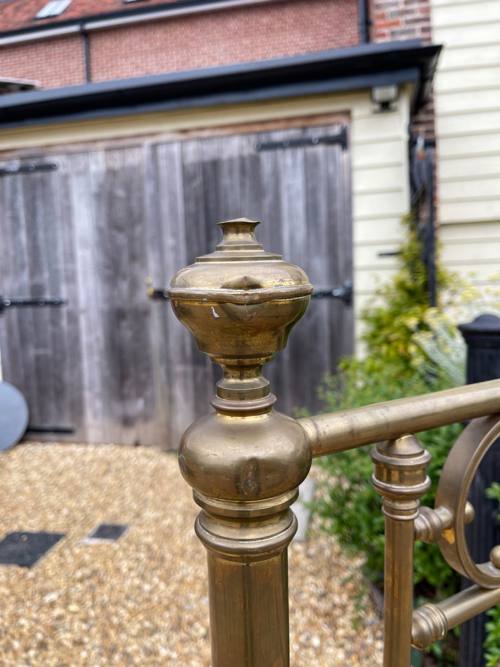 A Victorian single brass bed frame featuring a tall headboard and shorter footboard with turned finials and decorative circular ring inserts, set on castors. View IV
