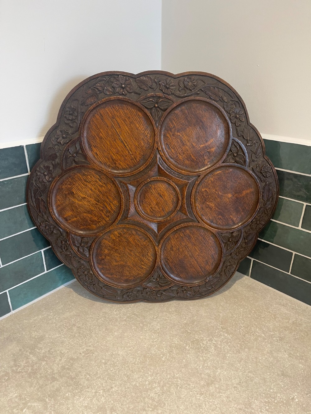A circular carved oak Lazy Susan featuring six outer recessed circular compartments, one central compartment, and a floral carved scalloped border.