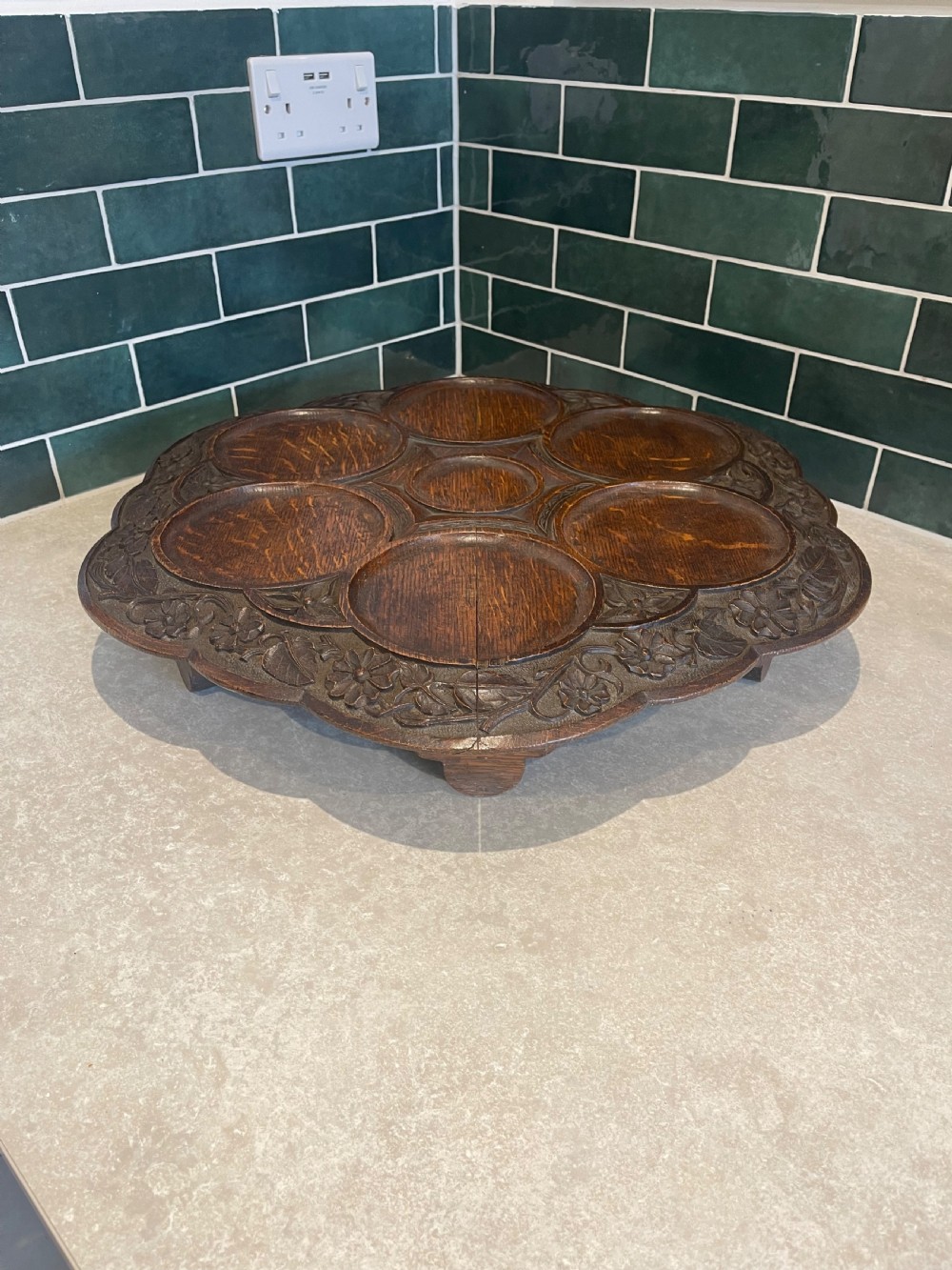 A circular carved oak Lazy Susan featuring six outer recessed circular compartments, one central compartment, and a floral carved scalloped border. View II