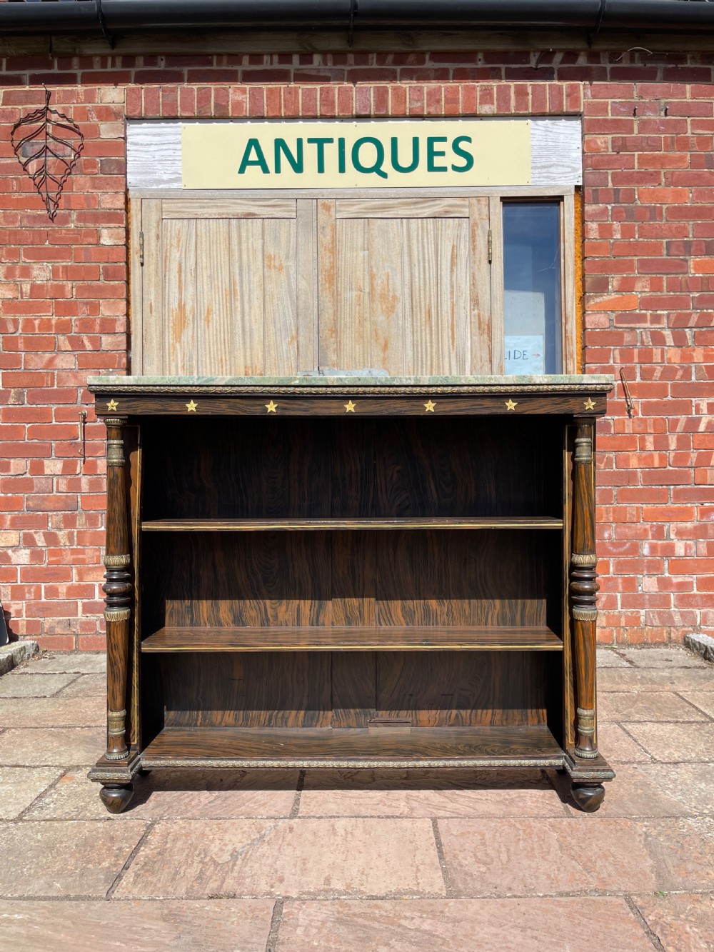 An early nineteenth-century open bookcase featuring a simulated rosewood painted finish, green marble top, gilt star motifs, and turned side columns.