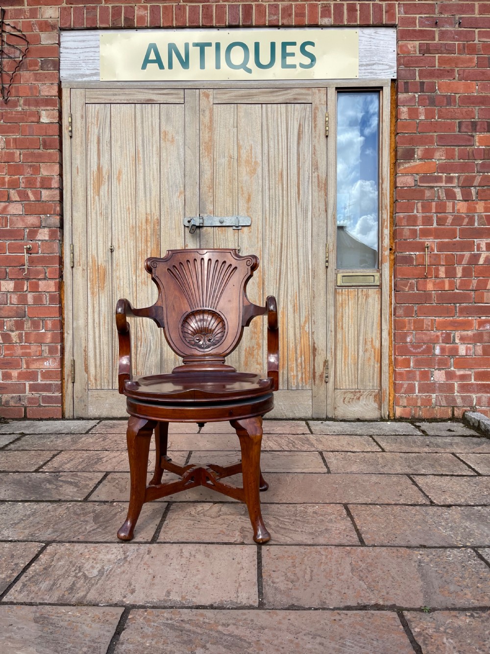 A late nineteenth-century carved mahogany revolving desk chair featuring a shell-carved backrest, curved armrests, a contoured wooden seat, and cabriole legs.