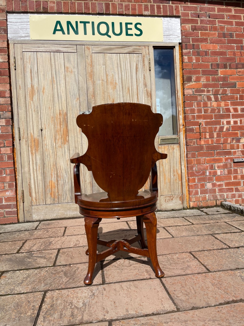 A late nineteenth-century carved mahogany revolving desk chair featuring a shell-carved backrest, curved armrests, a contoured wooden seat, and cabriole legs. View VI