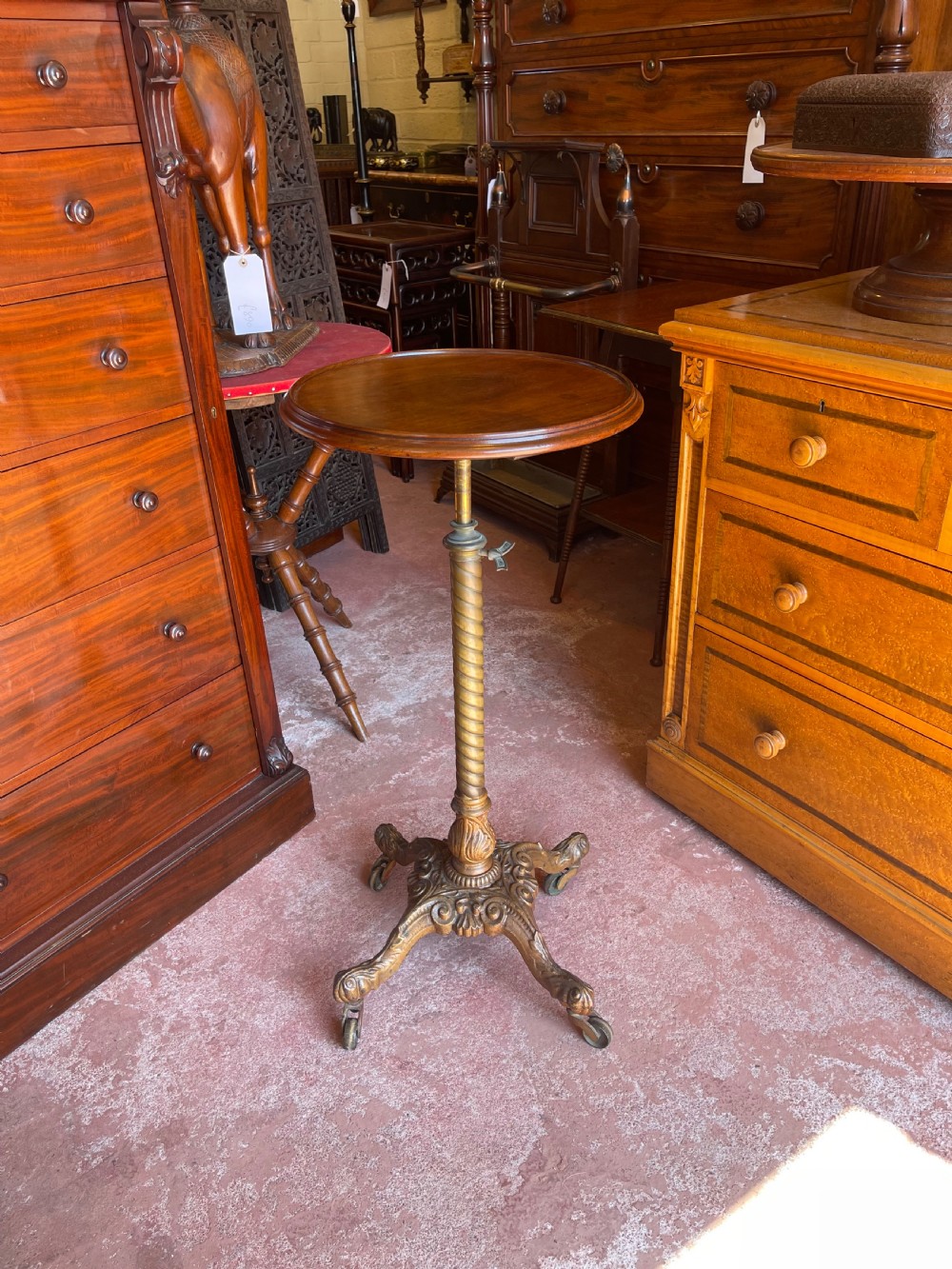 A nineteenth-century height-adjustable stand featuring a circular mahogany tabletop, a spiralled column with a wing nut mechanism, and an ornate cast metal base with castors.