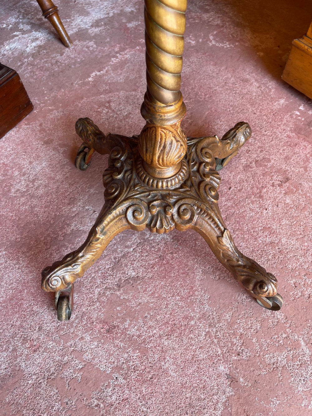 A nineteenth-century height-adjustable stand featuring a circular mahogany tabletop, a spiralled column with a wing nut mechanism, and an ornate cast metal base with castors. View II