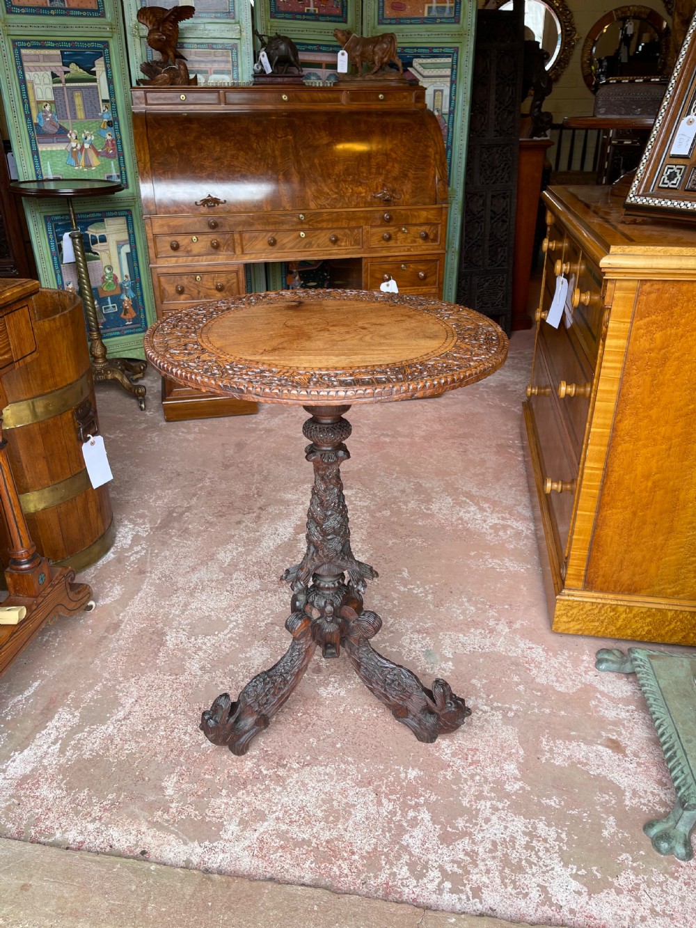 A round wooden pedestal table featuring hand-carved foliate borders and a sculpted tripod base.