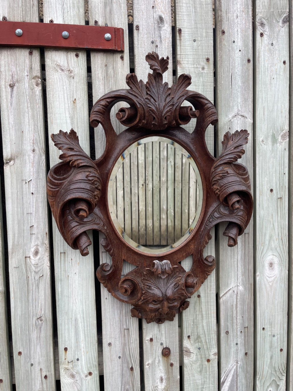A nineteenth-century carved oak wall mirror featuring an oval glass plate framed by ornate scrollwork, acanthus leaves, and a carved face at the base.