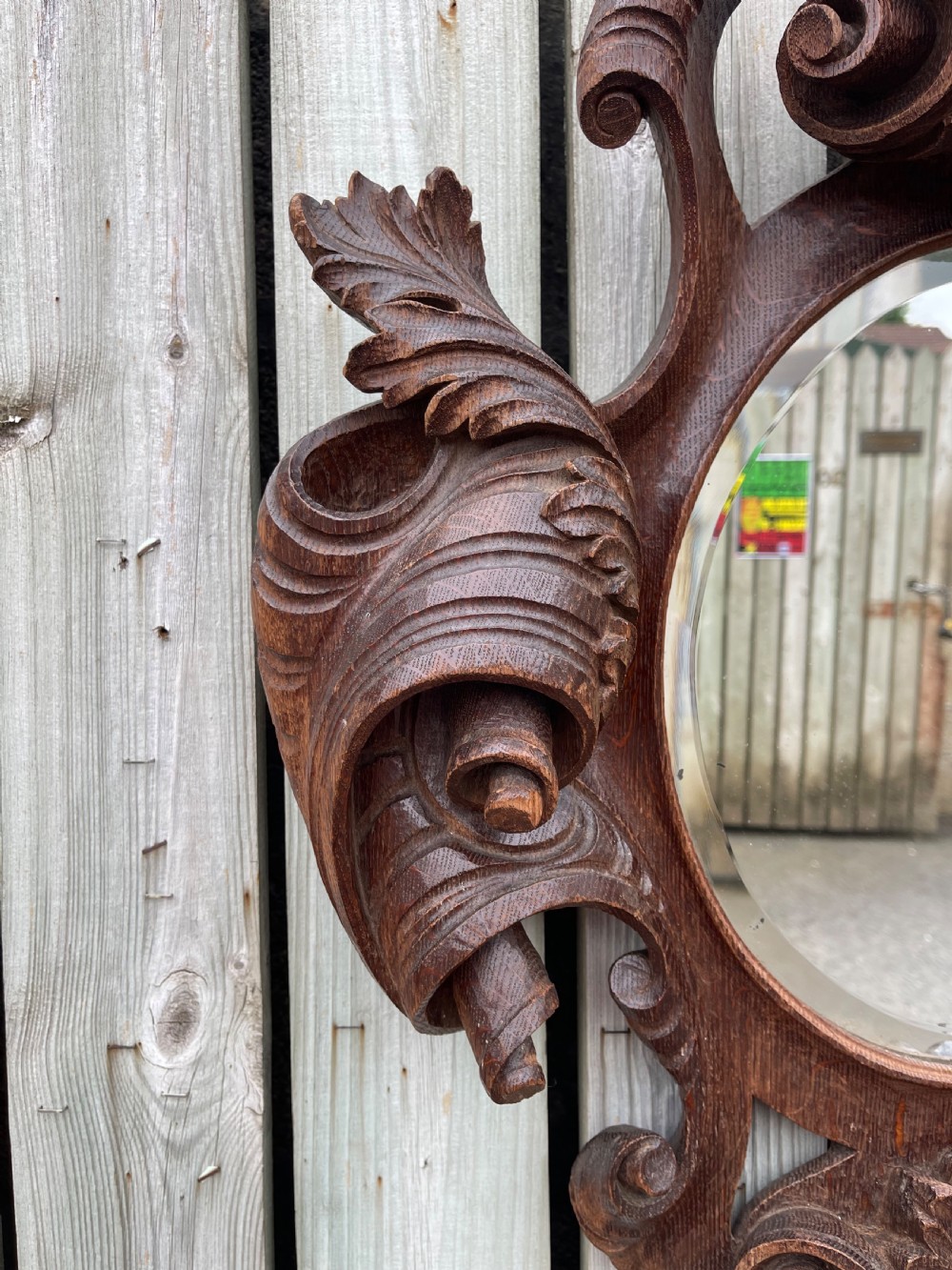 A nineteenth-century carved oak wall mirror featuring an oval glass plate framed by ornate scrollwork, acanthus leaves, and a carved face at the base. View II