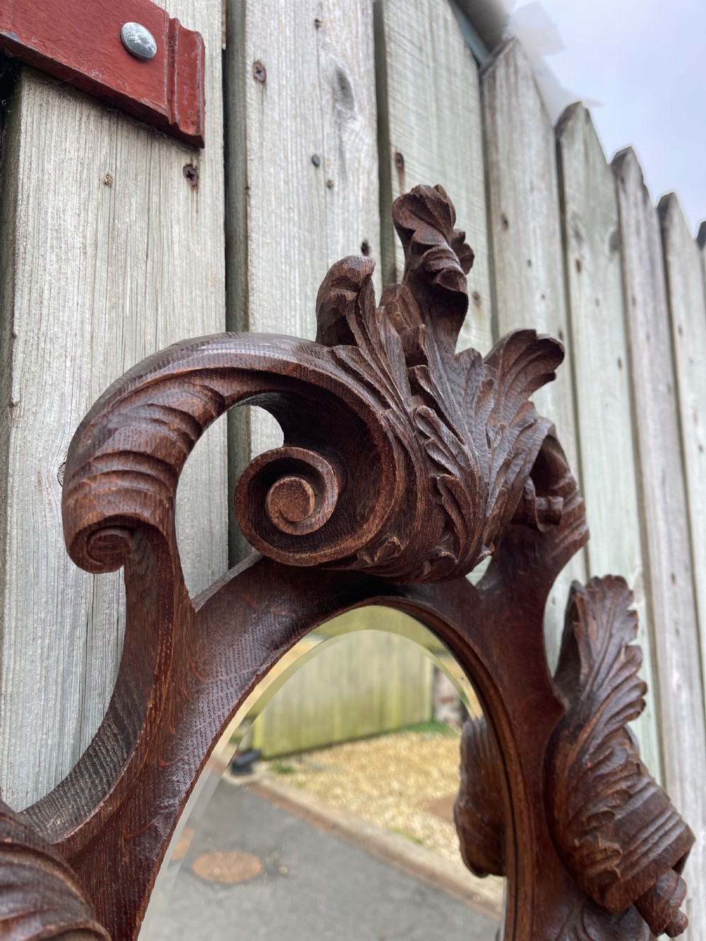 A nineteenth-century carved oak wall mirror featuring an oval glass plate framed by ornate scrollwork, acanthus leaves, and a carved face at the base. View IV