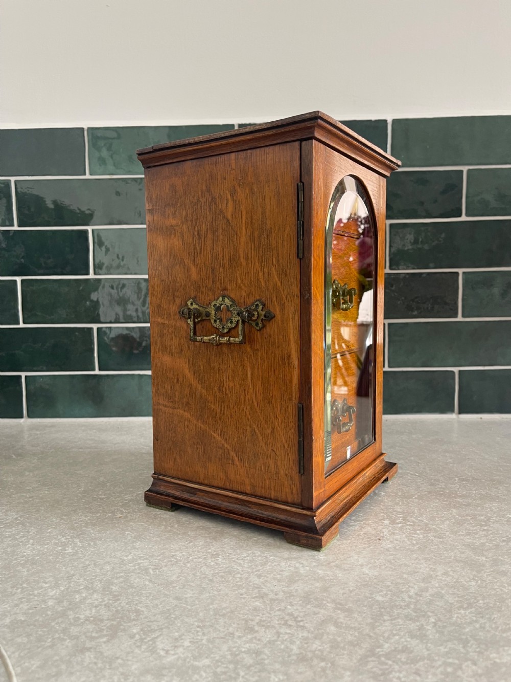 A 19th-century oak tabletop cabinet featuring three internal drawers behind an arched glazed door with decorative brass drop handles. View V