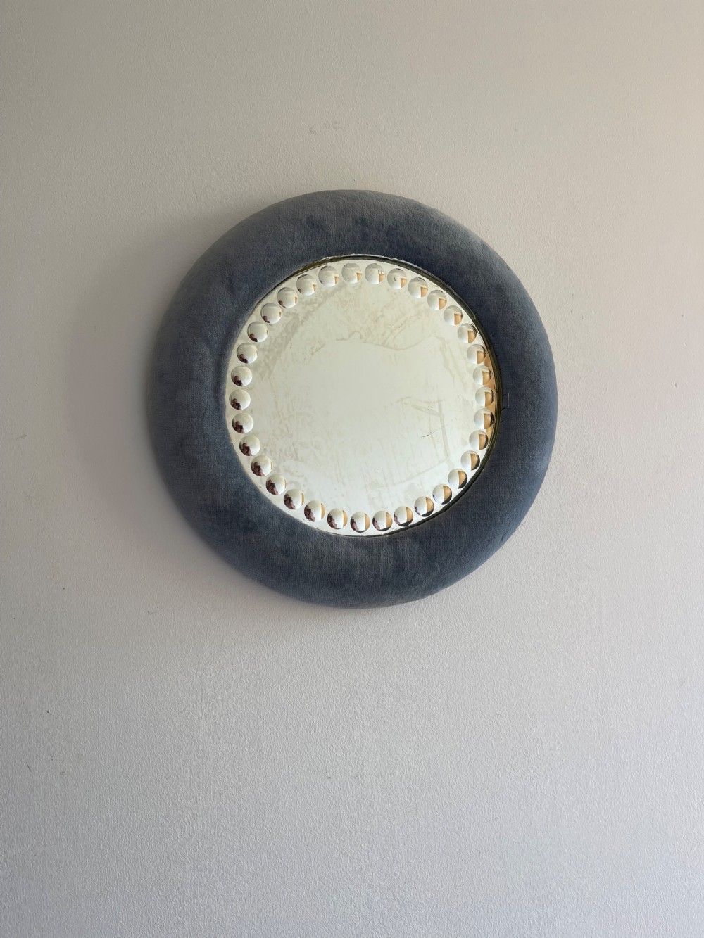 A circular convex sorcerer wall mirror featuring a padded grey velvet outer frame and an inner border of glass cabochons.