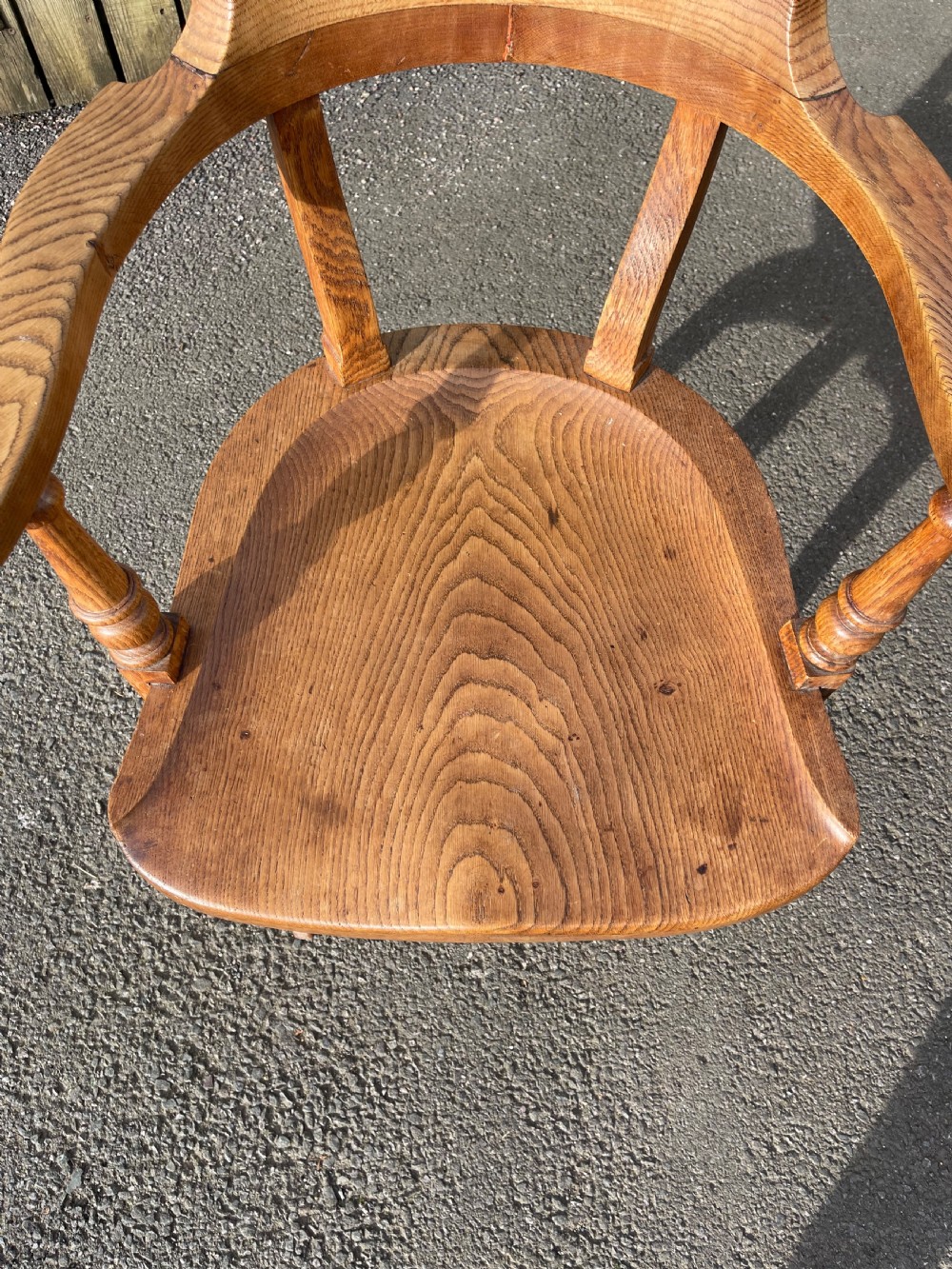 An antique golden oak revolving desk chair featuring curved armrests, a contoured wooden seat, and a four-legged base on castors. View II