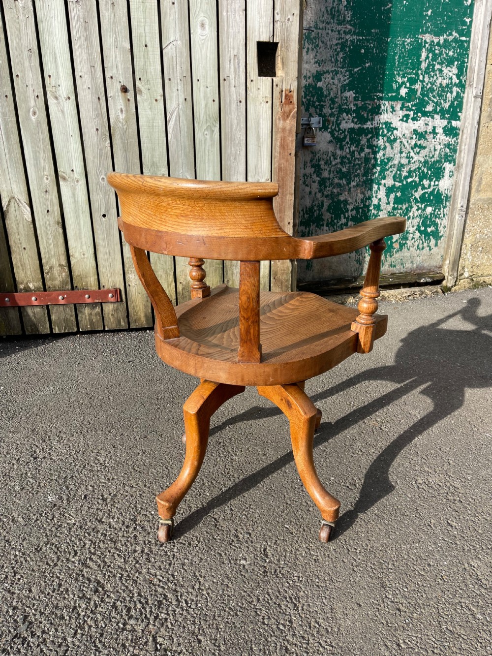 An antique golden oak revolving desk chair featuring curved armrests, a contoured wooden seat, and a four-legged base on castors. View III