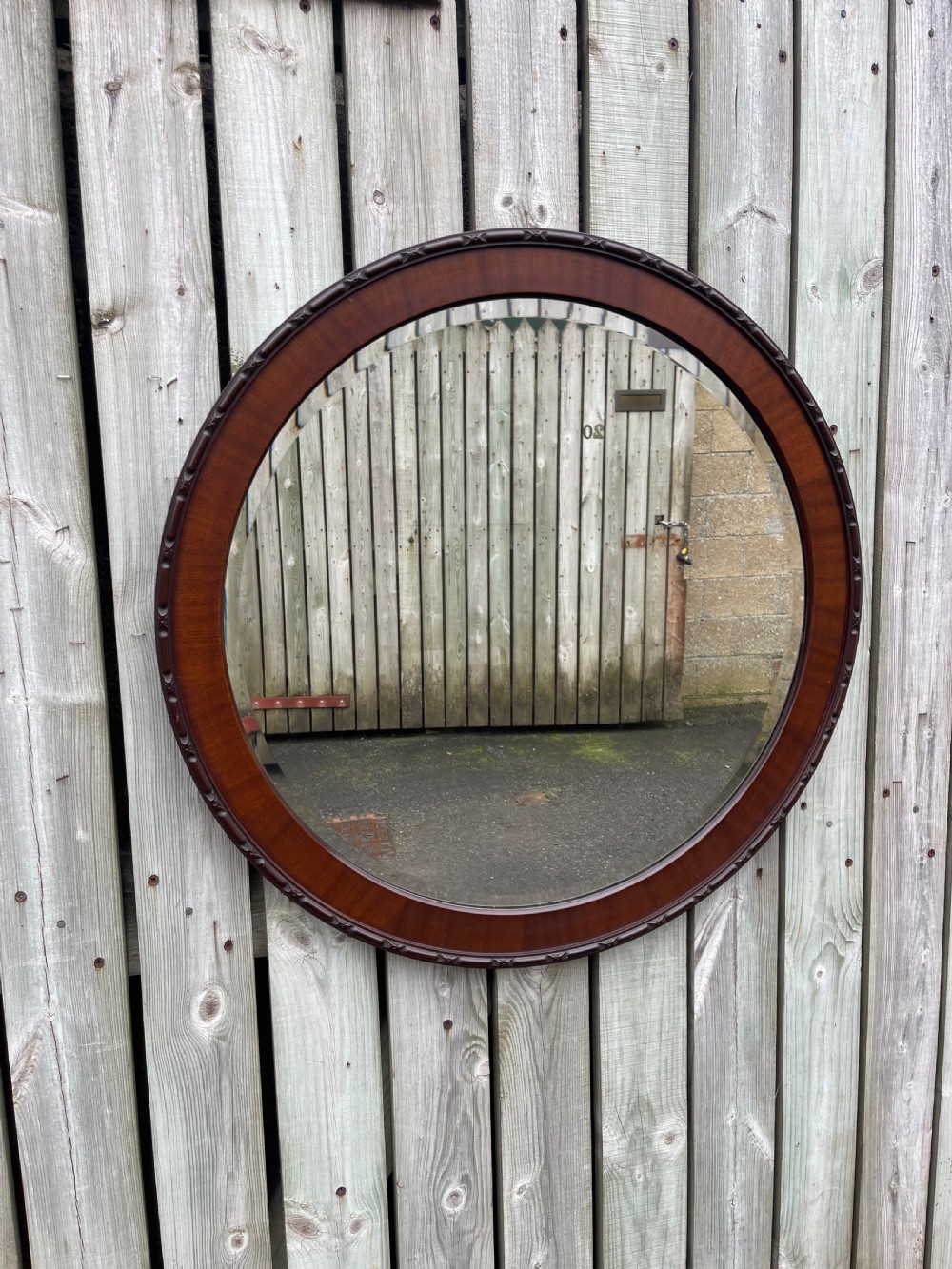 A large circular wall mirror featuring a polished mahogany wooden frame with carved edge detail and a bevelled glass plate.