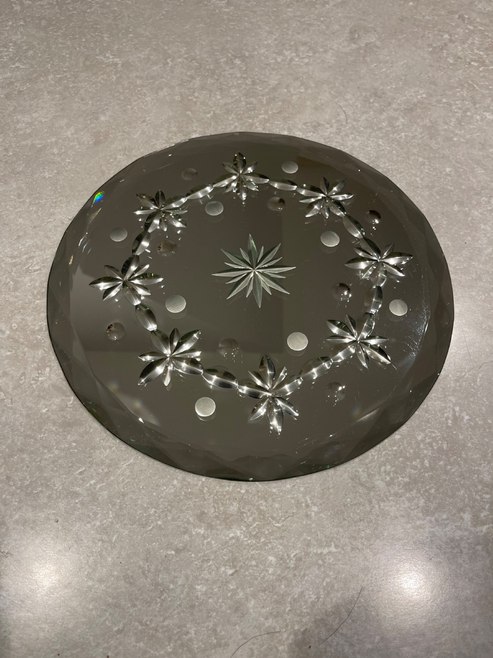 A circular bevelled glass mirror plate decorated with cut starburst and floral wheel motifs around the perimeter.