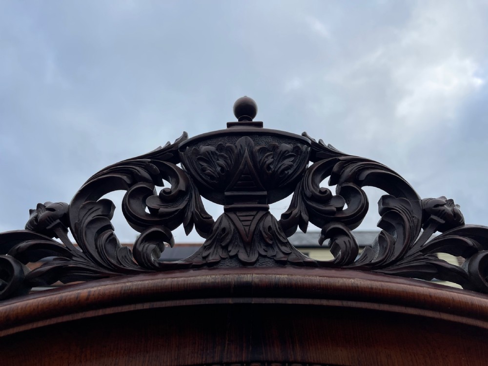 A tall dark rosewood Continental display cabinet featuring arched glazed double doors, an intricate carved pediment cresting, and a lower drawer. View III