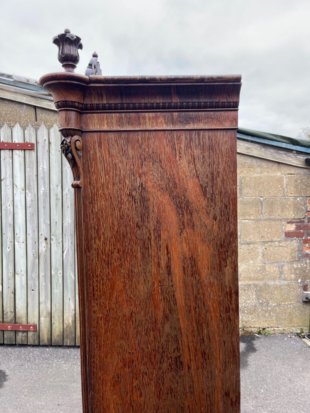 A tall dark rosewood Continental display cabinet featuring arched glazed double doors, an intricate carved pediment cresting, and a lower drawer. View VII