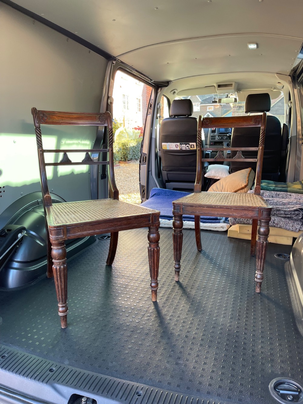 A pair of antique Regency style dark mahogany side chairs featuring carved top rails, woven cane seats, and reeded front legs.