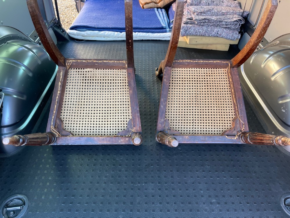 A pair of antique Regency style dark mahogany side chairs featuring carved top rails, woven cane seats, and reeded front legs. View VIII