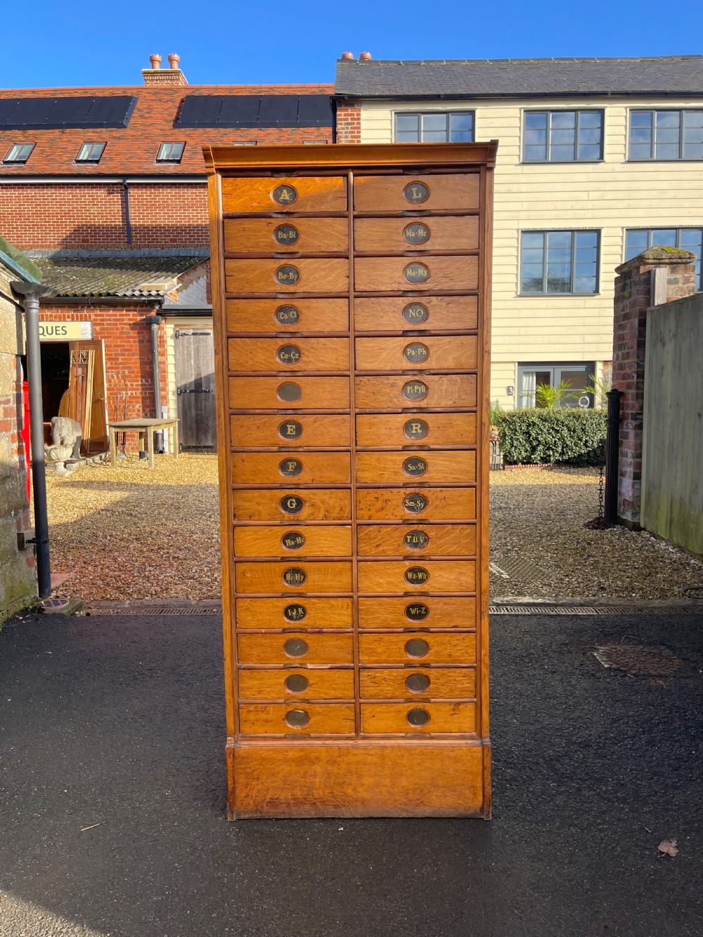 A tall Victorian golden oak Amberg patent filing cabinet featuring twin vertical columns of index drawers marked with alphabetical labels.